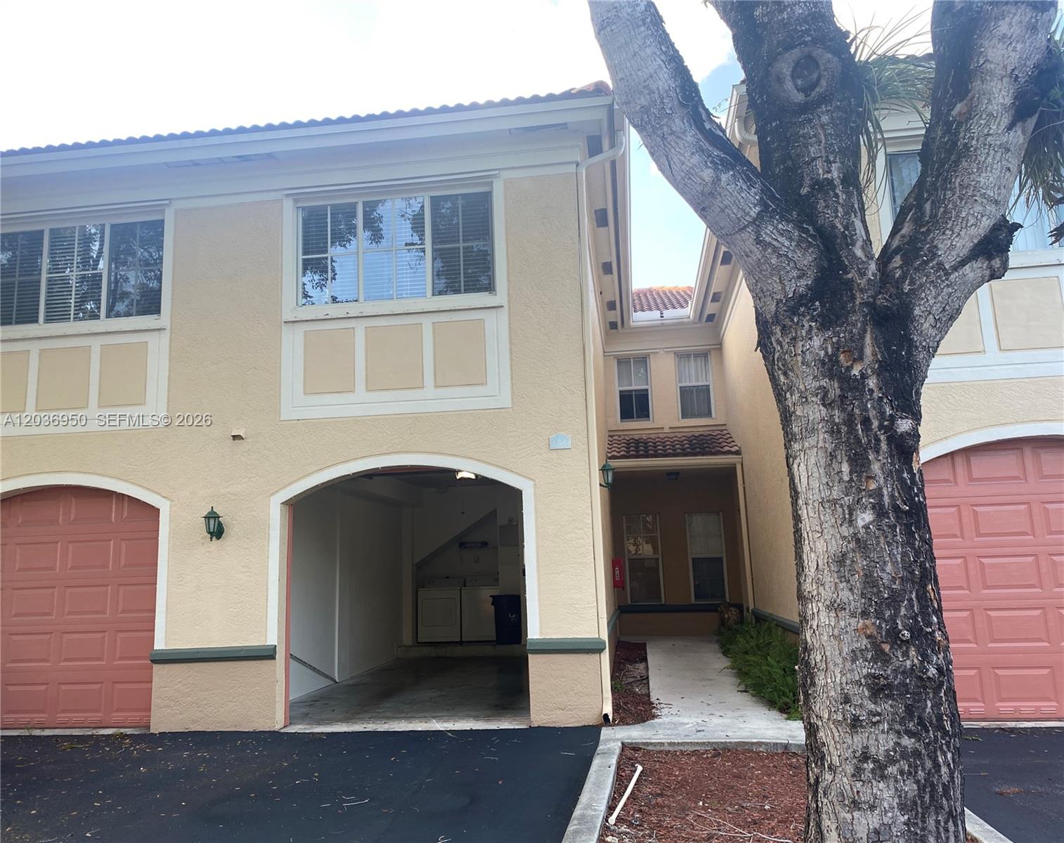 The exterior of a two-story townhouse features a garage, a walkway, and a large tree — 2492 Centergate Dr # 102, Miramar FL 33025, MIRAMAR, FL