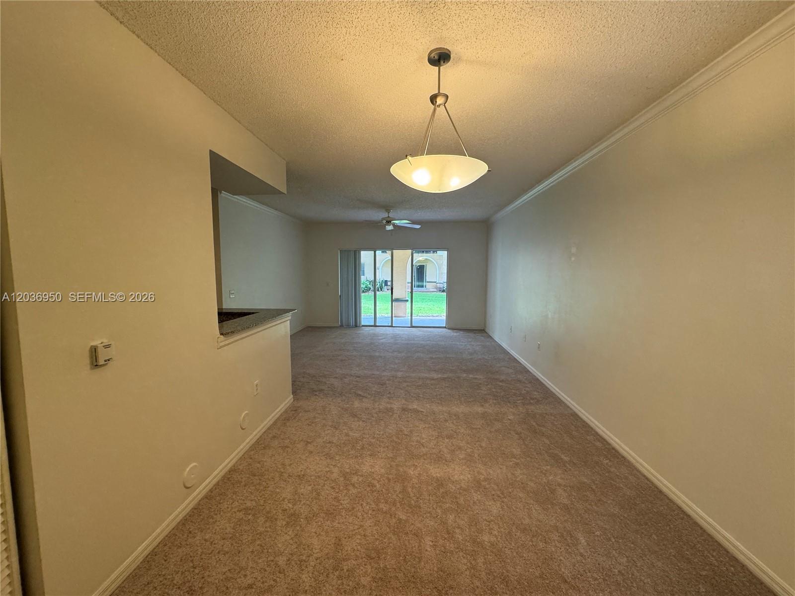 An empty living room features beige carpeting, a pendant light, and sliding glass patio doors — 2492 Centergate Dr # 102, Miramar FL 33025, MIRAMAR, FL