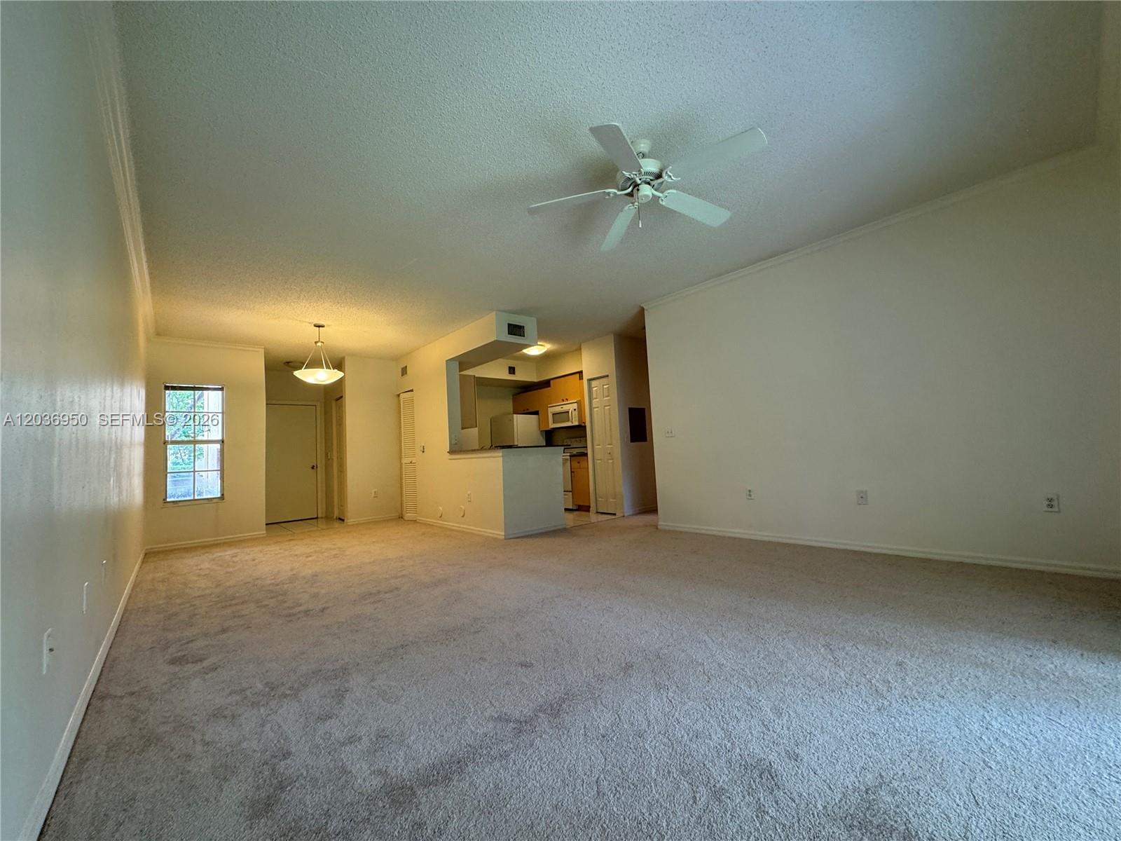A carpeted living room features a ceiling fan and an open kitchen with light-colored cabinets — 2492 Centergate Dr # 102, Miramar FL 33025, MIRAMAR, FL