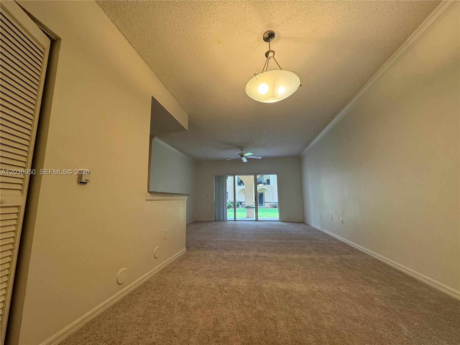 An empty living room features beige carpeting, a ceiling fan, and sliding glass patio doors — 2492 Centergate Dr # 102, Miramar FL 33025, MIRAMAR, FL