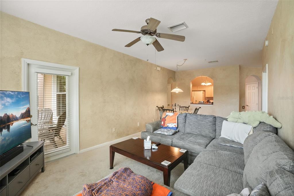 A living room with a gray sectional sofa, coffee table, television, and a dining area beyond — 13500 TURTLE MARSH LOOP UNIT 823, ORLANDO, FL