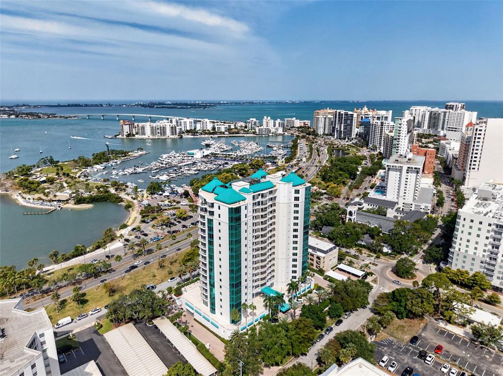 An aerial view shows a tall, teal-roofed residential building near a marina and coastal bridge — 340 S PALM AVENUE UNIT 14, SARASOTA, FL