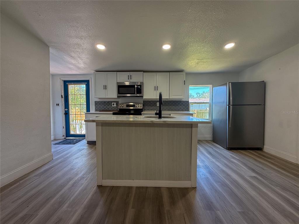 A kitchen features white cabinets, a central island with a sink, and stainless steel appliances — 18920 3RD AVENUE, ORLANDO, FL