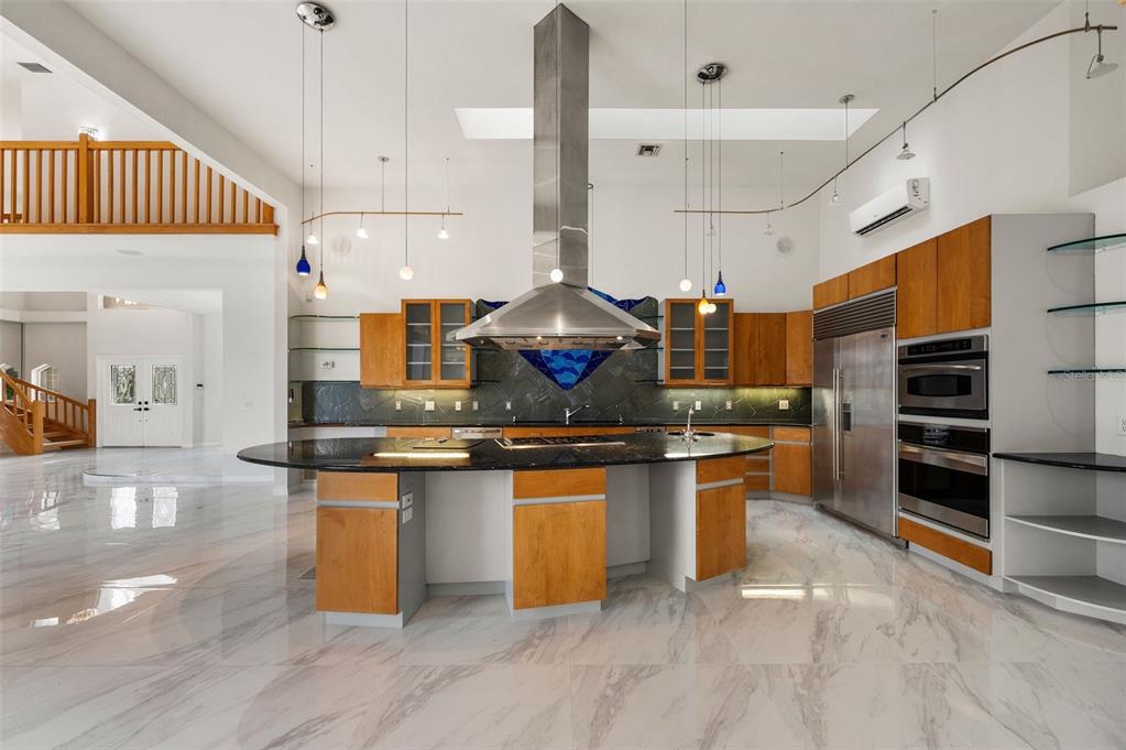 A modern kitchen features wood cabinetry, a large curved island, and stainless steel appliances — 4323 ROCK CREEK DRIVE, PORT CHARLOTTE, FL