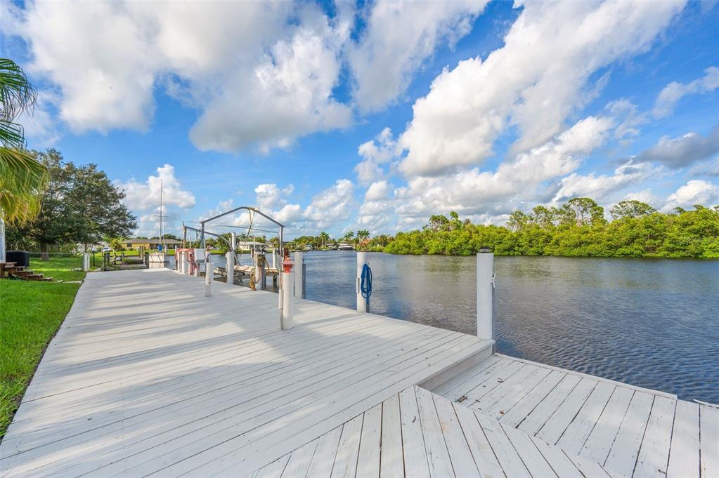 A white wooden boat dock extends over a canal toward a line of green trees — 4323 ROCK CREEK DRIVE, PORT CHARLOTTE, FL