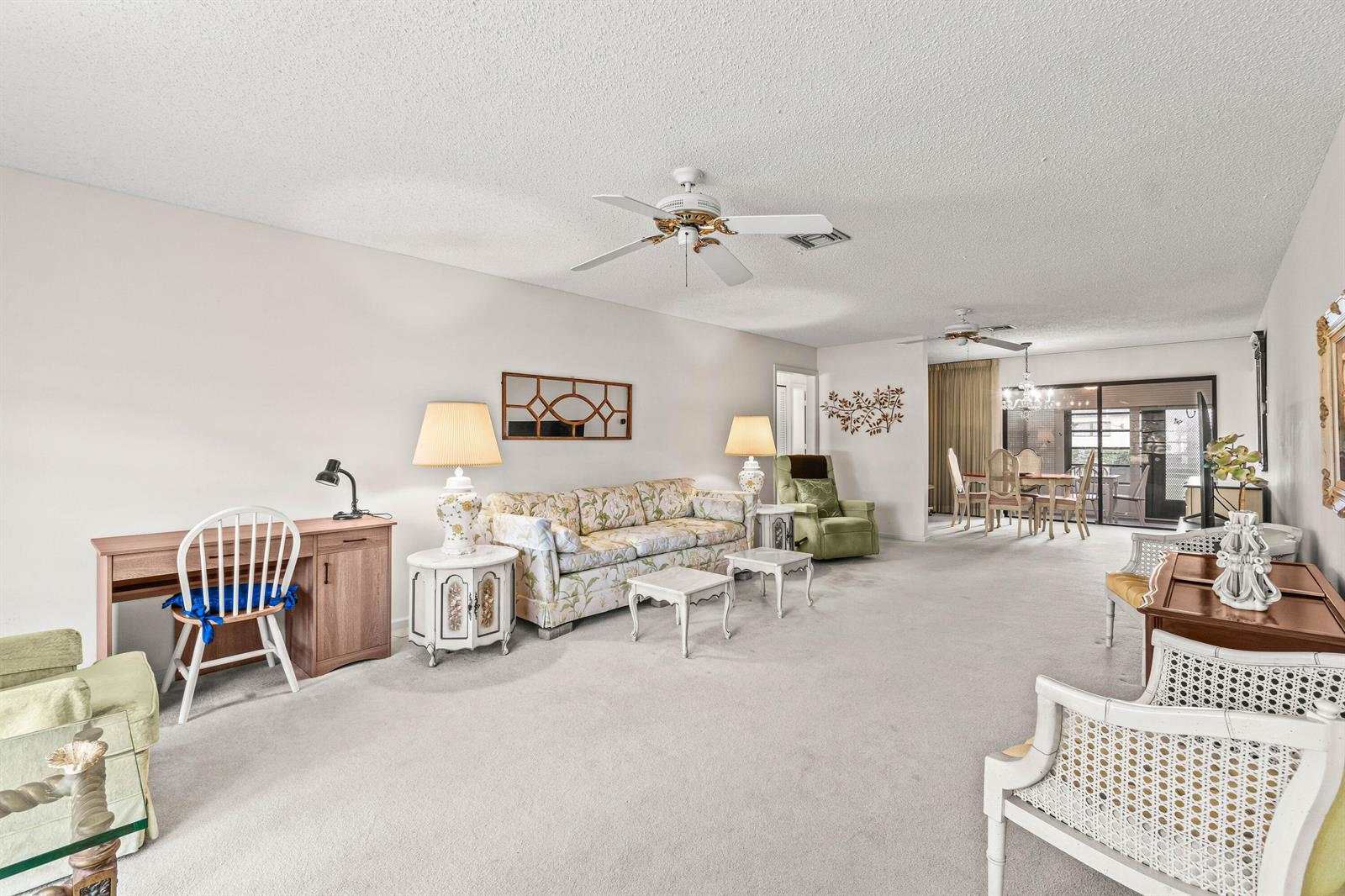 A spacious living room features light carpeting, a floral sofa, and a dining area beyond — 4868 Hawkwood Road # A, Boynton Beach FL 33436, BOYNTON BEACH, FL