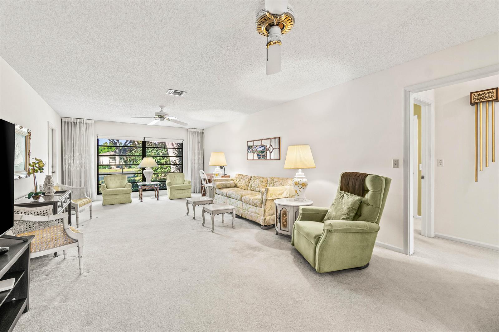 A living room features light carpeting, a floral sofa, green armchairs, and a ceiling fan — 4868 Hawkwood Road # A, Boynton Beach FL 33436, BOYNTON BEACH, FL