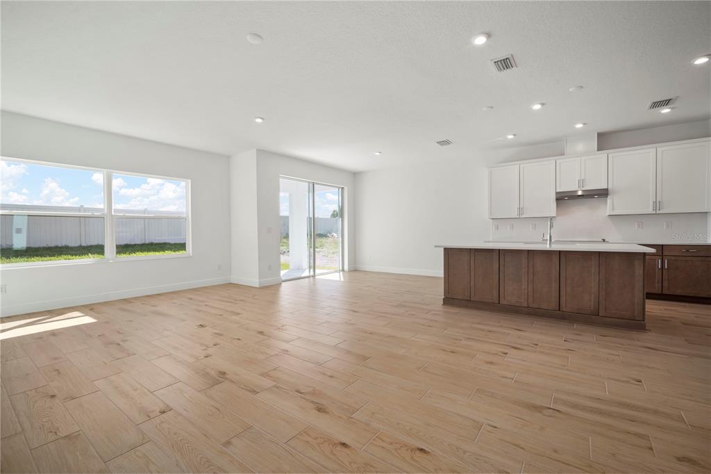 A bright, open-concept kitchen and living area features light wood-look tile flooring and white cabinetry — 2945 STEWART CREEK CIRCLE, PLANT CITY, FL