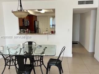 A dining area with a glass table and black chairs overlooks a kitchen pass-through window — 1100 NE 191st St # 24E, Miami FL 33179, MIAMI, FL