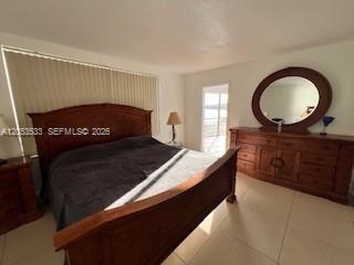 A bedroom features a large wooden bed frame, a matching dresser with a mirror, and tile flooring — 1100 NE 191st St # 24E, Miami FL 33179, MIAMI, FL