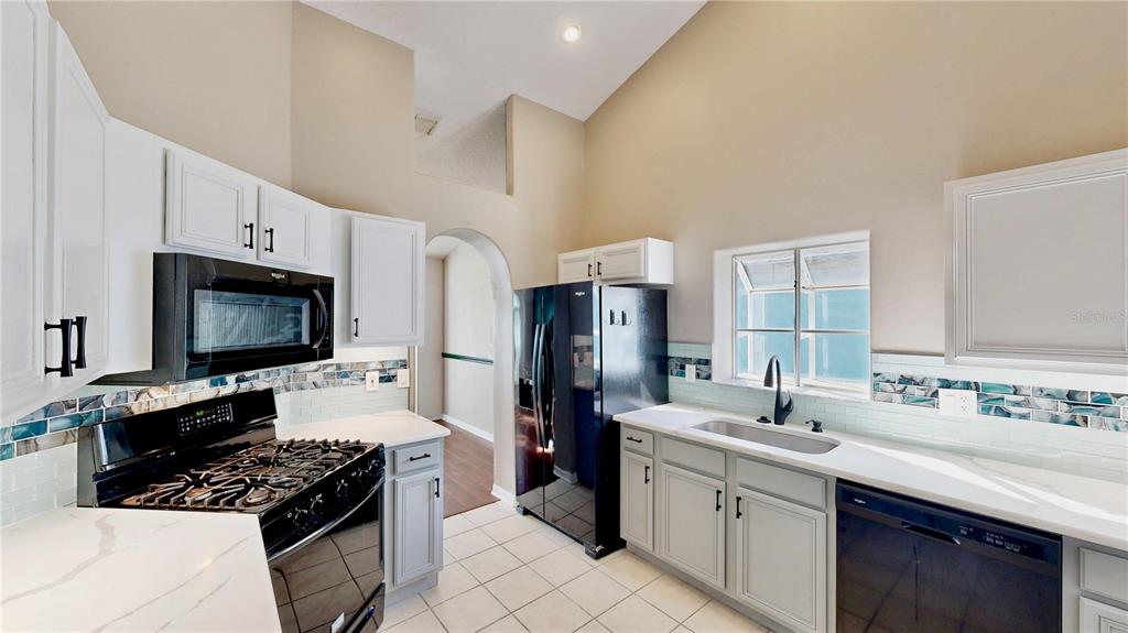 A kitchen features white cabinets, black appliances, a tiled backsplash, and a high vaulted ceiling — 3016 CRYSTAL CREEK BOULEVARD, ORLANDO, FL