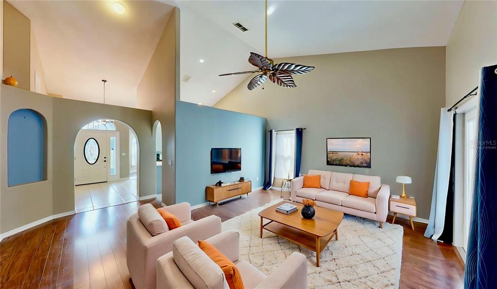 A living room features a vaulted ceiling, light-colored furniture, a blue accent wall, and hardwood floors — 3016 CRYSTAL CREEK BOULEVARD, ORLANDO, FL