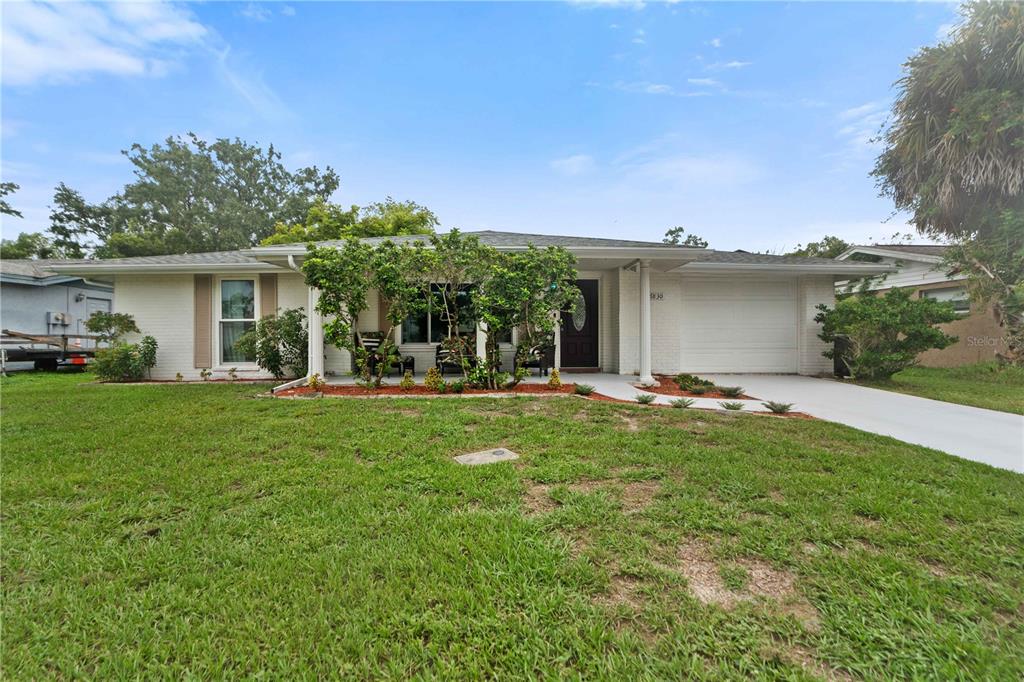 A single-story white brick house with a front porch, attached garage, and green lawn — 7830 CHERRYTREE LANE, NEW PORT RICHEY, FL