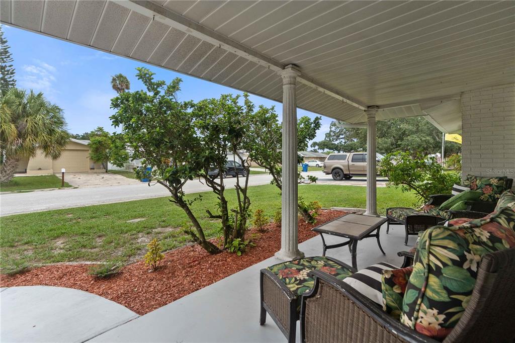 A covered porch features wicker furniture with floral cushions and a view of the street — 7830 CHERRYTREE LANE, NEW PORT RICHEY, FL