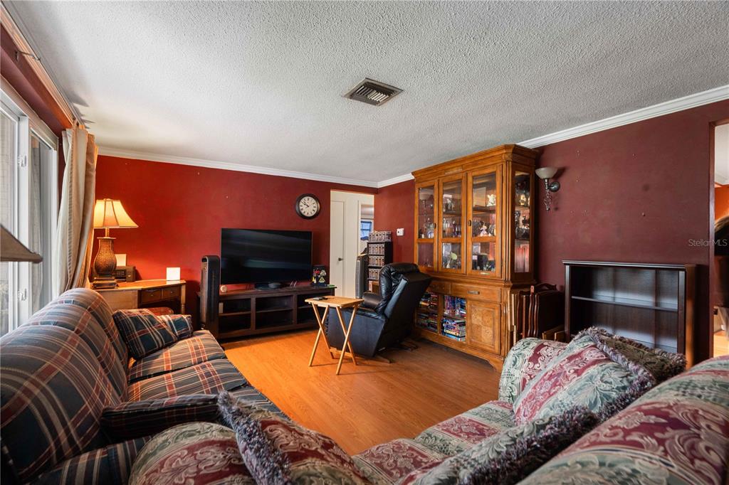 A living room with red walls, wood flooring, a plaid sofa, and a large wooden hutch — 7830 CHERRYTREE LANE, NEW PORT RICHEY, FL