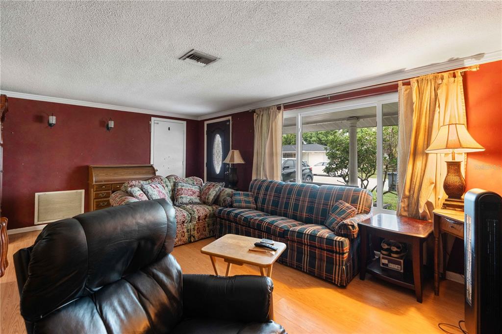 A living room with red walls, wood flooring, a plaid sofa, and a large window — 7830 CHERRYTREE LANE, NEW PORT RICHEY, FL
