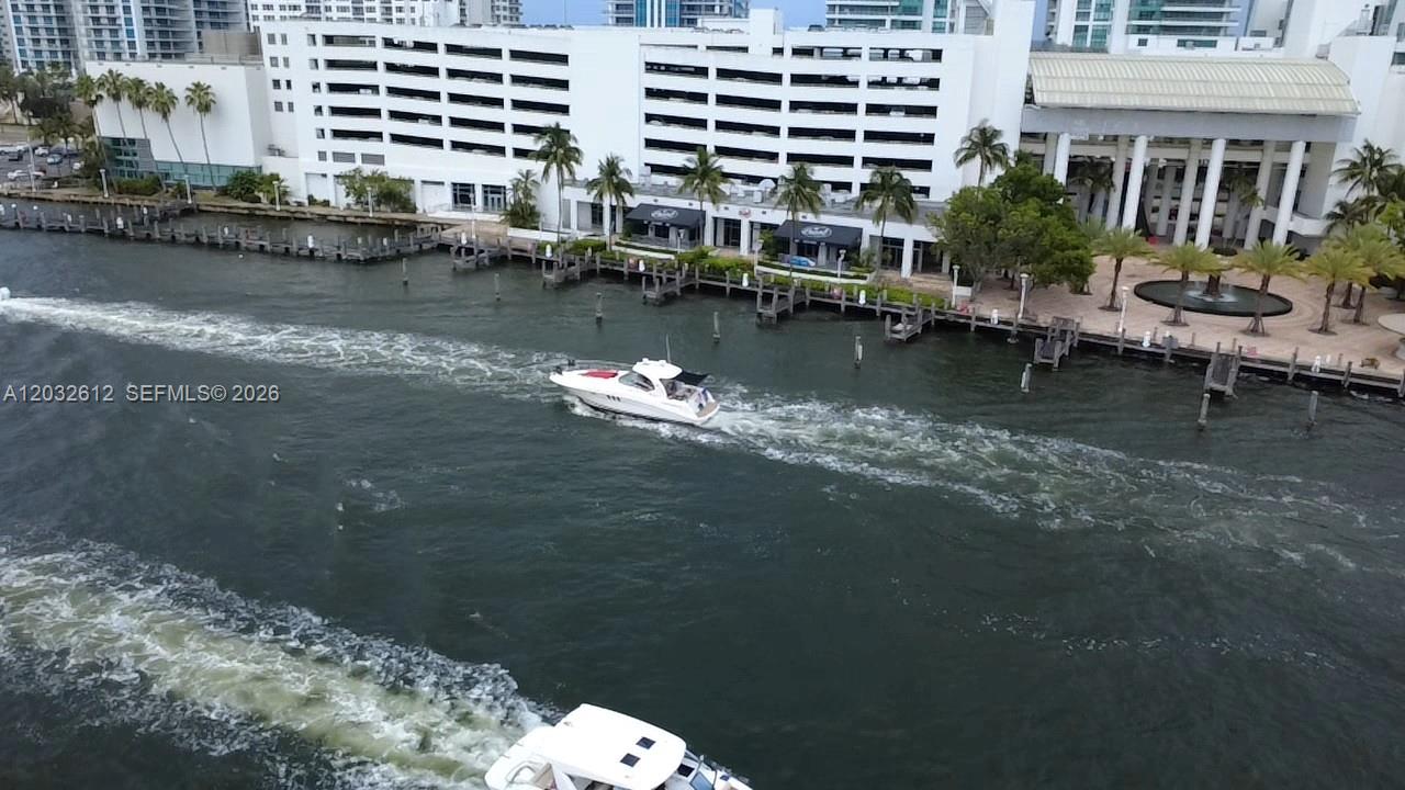 An aerial view shows a white motorboat cruising on a waterway past a large building — 400 Leslie Dr # 1124, Hallandale Beach FL 33009, HALLANDALE BEACH, FL