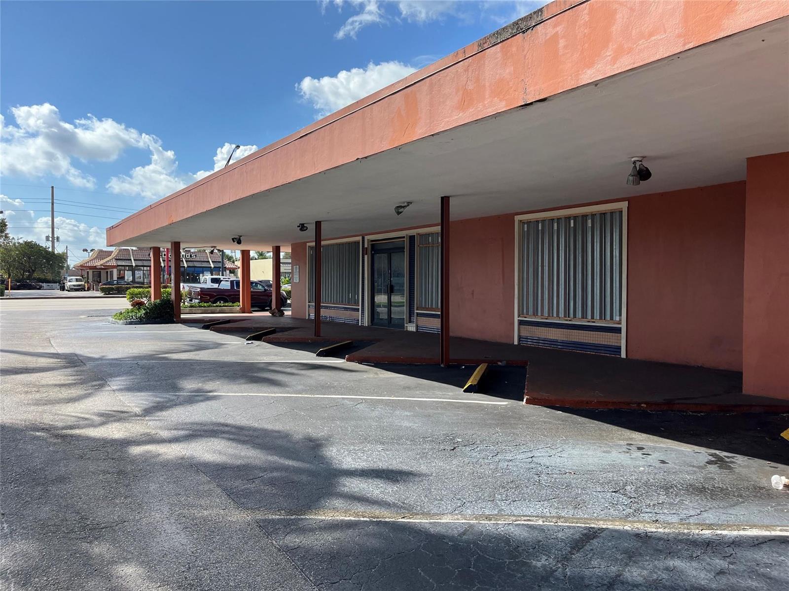 A low-slung, salmon-colored commercial building features a covered walkway and parking spaces in front — 1361 E Commercial Boulevard, Oakland Park FL 33334, OAKLAND PARK, FL