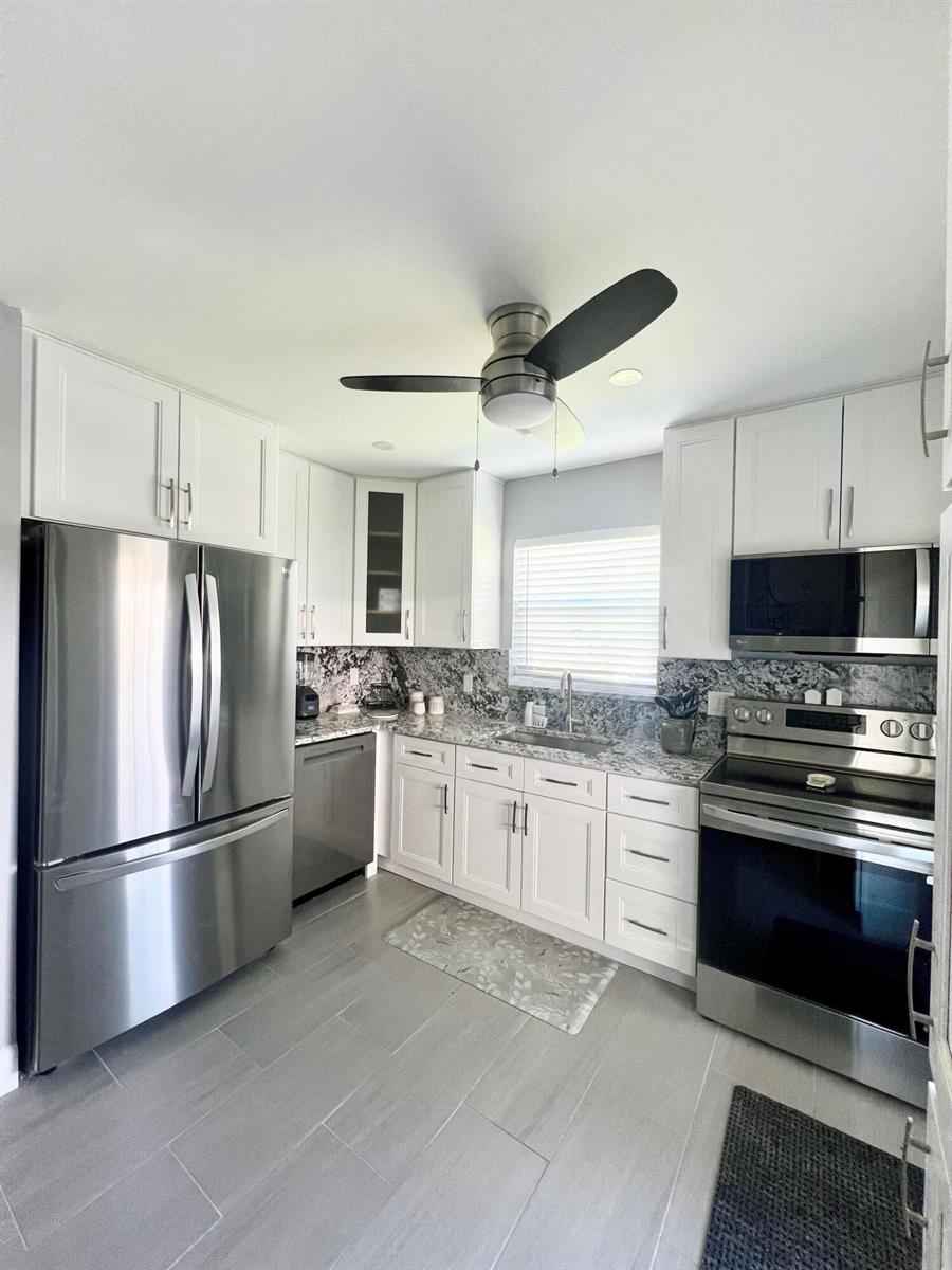 A kitchen features white cabinets, stainless steel appliances, granite countertops, and gray tile flooring — 222 SE 3rd Street, Boynton Beach FL 33435, BOYNTON BEACH, FL