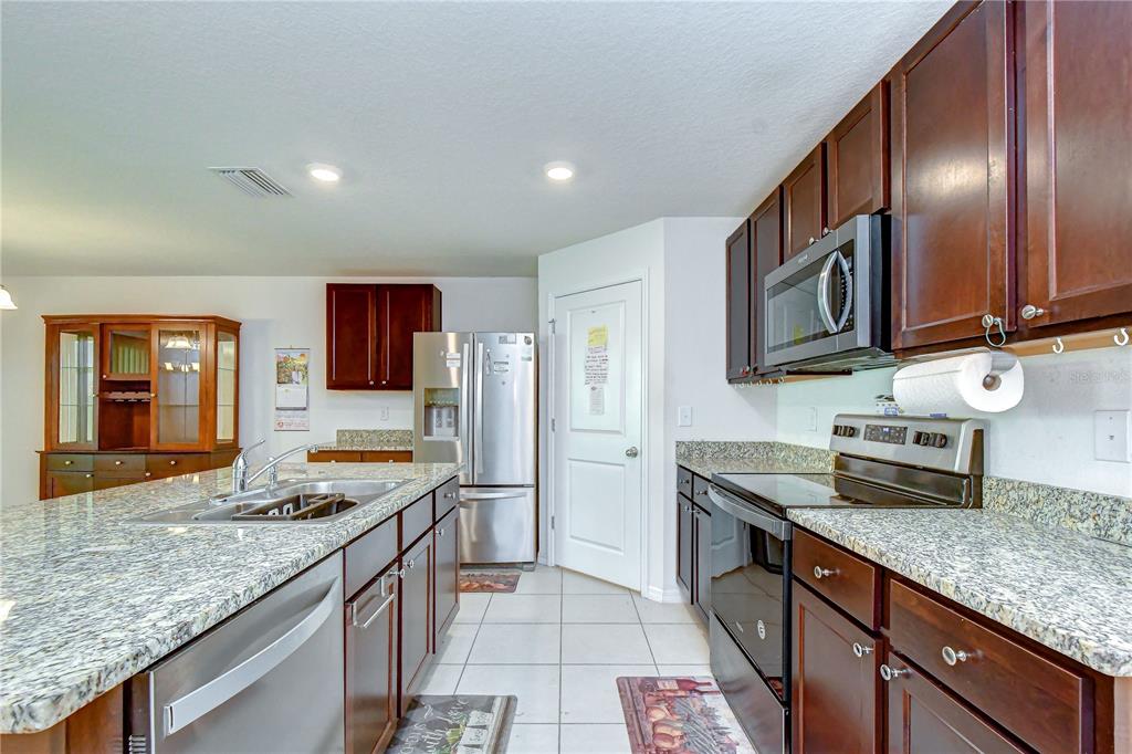 A kitchen features dark wood cabinets, granite countertops, stainless steel appliances, and a center island — 7760 BROAD POINTE DRIVE, ZEPHYRHILLS, FL