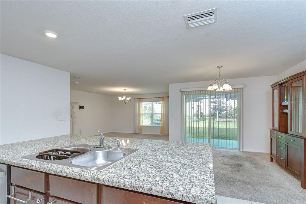 A kitchen island with a granite countertop and sink overlooks a dining area and living room — 7760 BROAD POINTE DRIVE, ZEPHYRHILLS, FL