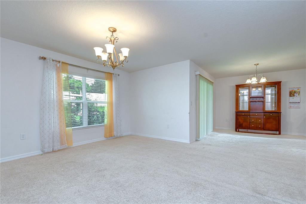 A dining room with beige carpet, a chandelier, a window with curtains, and a wooden hutch — 7760 BROAD POINTE DRIVE, ZEPHYRHILLS, FL
