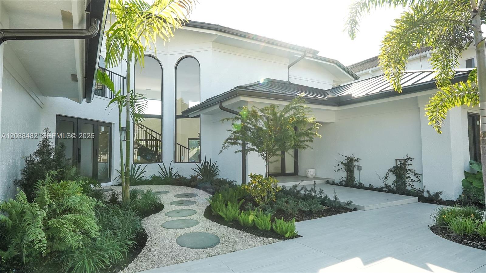The exterior of a white house features a stone path, landscaping, and tall arched windows — 7190 Valencia Dr, Boca Raton FL 33433, BOCA RATON, FL