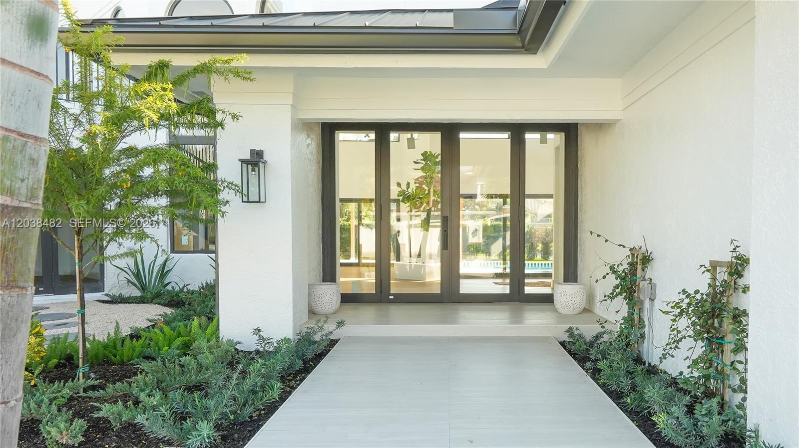 A modern home entrance features a glass-paneled door, white exterior walls, and landscaped garden beds — 7190 Valencia Dr, Boca Raton FL 33433, BOCA RATON, FL