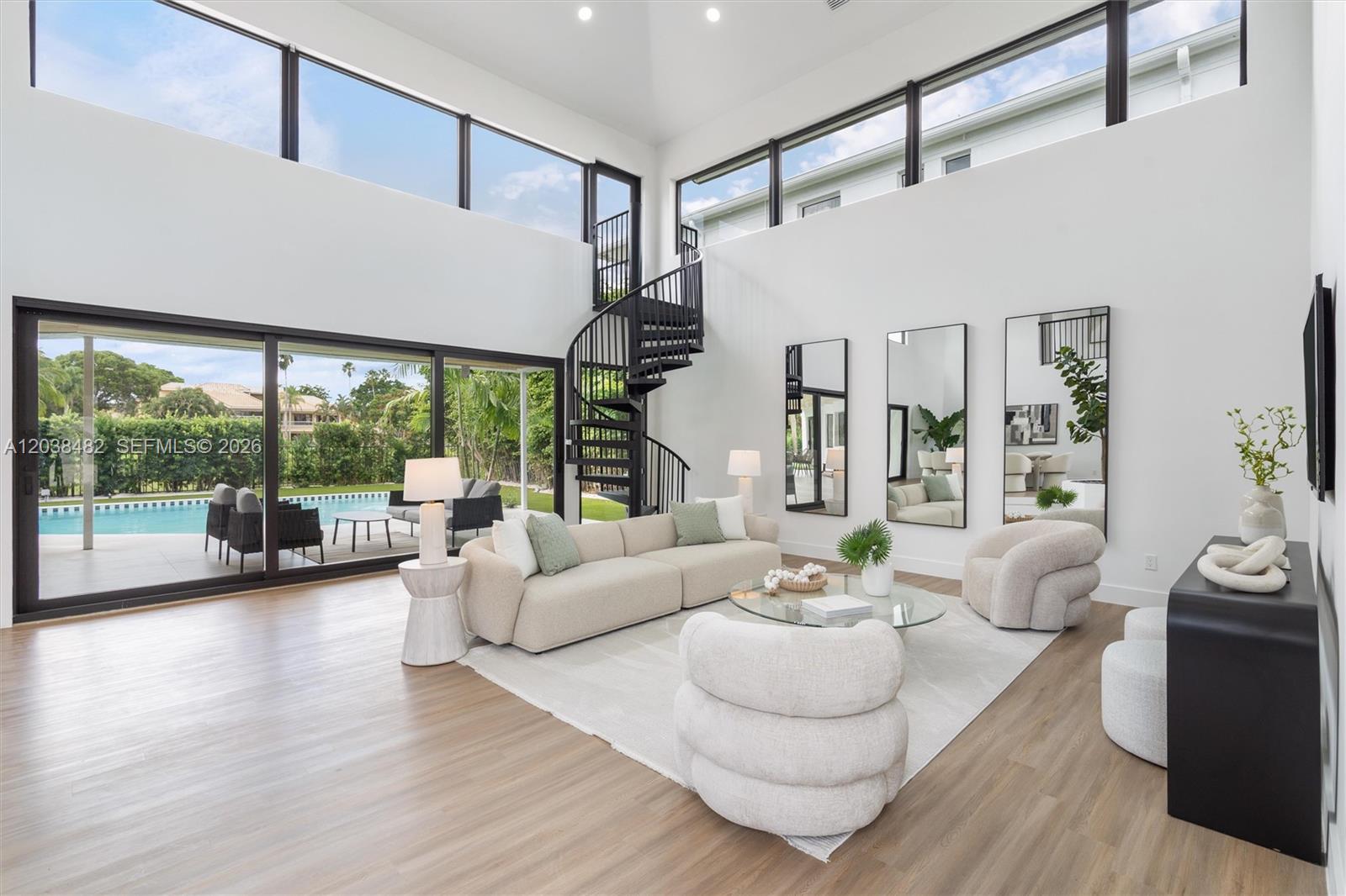 A modern living room features a spiral staircase, floor-to-ceiling windows, and a view of a pool — 7190 Valencia Dr, Boca Raton FL 33433, BOCA RATON, FL