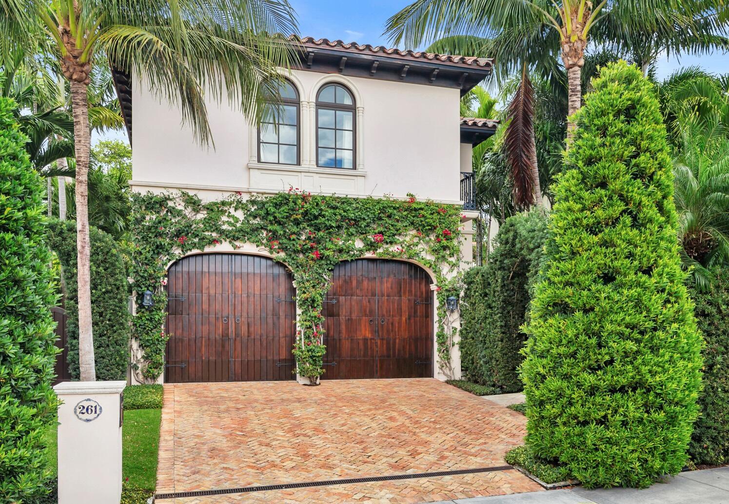 A two-story house features two arched wooden garage doors covered in climbing vines and bougainvillea — 261 Seminole Avenue, Palm Beach FL 33480, PALM BEACH, FL