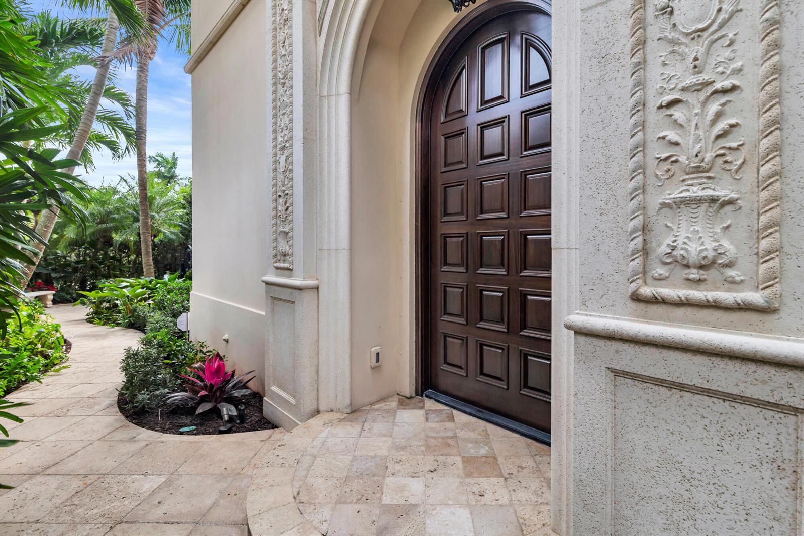 A dark wood arched door is set into a stone entryway with decorative wall carvings — 261 Seminole Avenue, Palm Beach FL 33480, PALM BEACH, FL