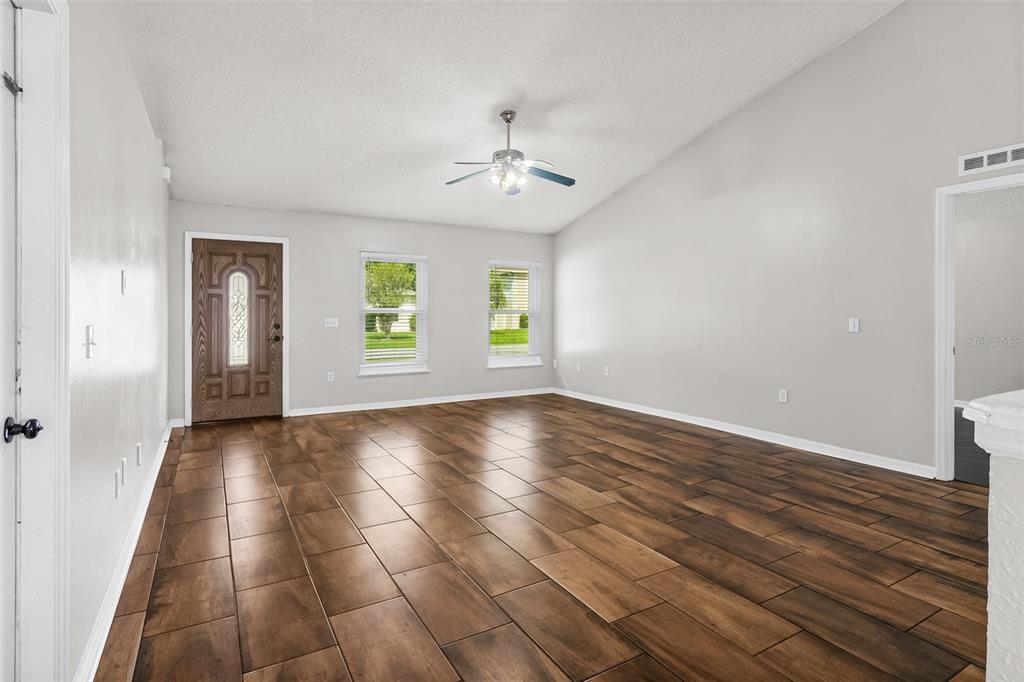 An empty living room features wood-look tile flooring, light gray walls, and a ceiling fan — 51 BEAVERDAM LANE, PALM COAST, FL