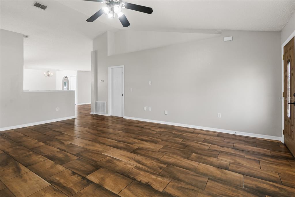 A spacious living room features light gray walls, vaulted ceilings, and dark wood-look tile flooring — 51 BEAVERDAM LANE, PALM COAST, FL