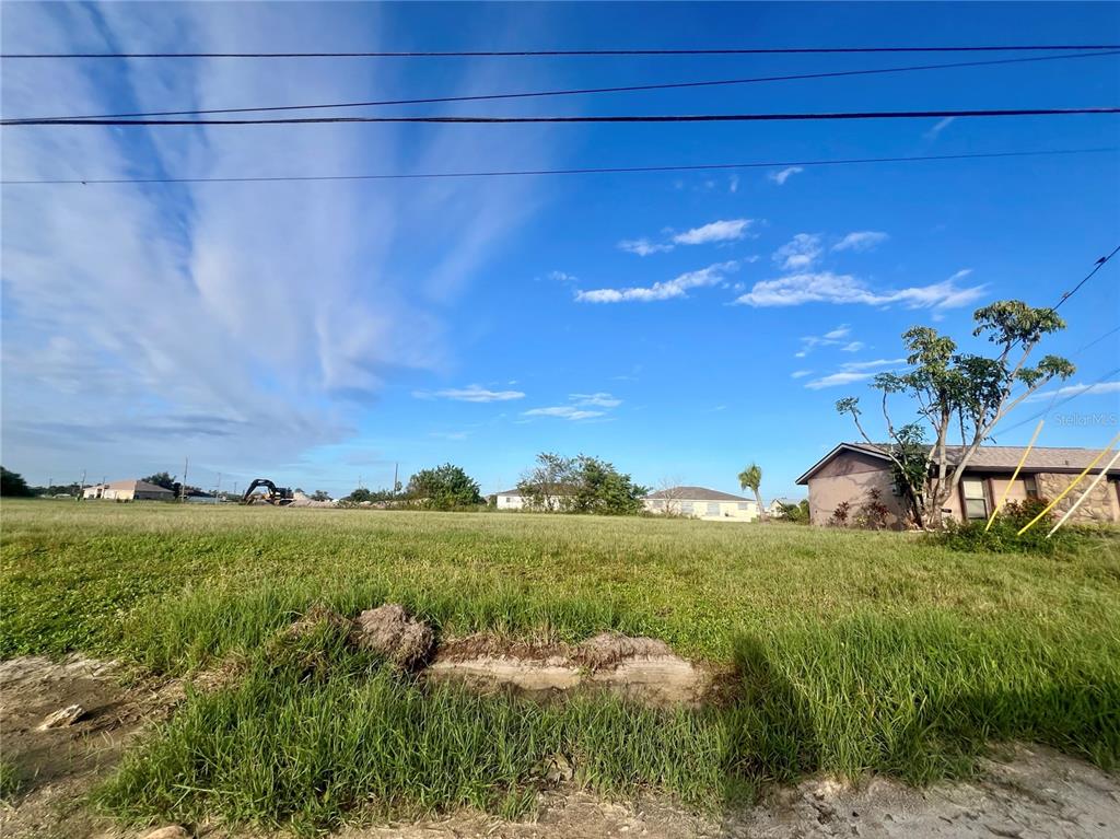 A grassy vacant lot sits in front of a residential house under a blue sky — 1424 NE 9TH AVENUE, CAPE CORAL, FL