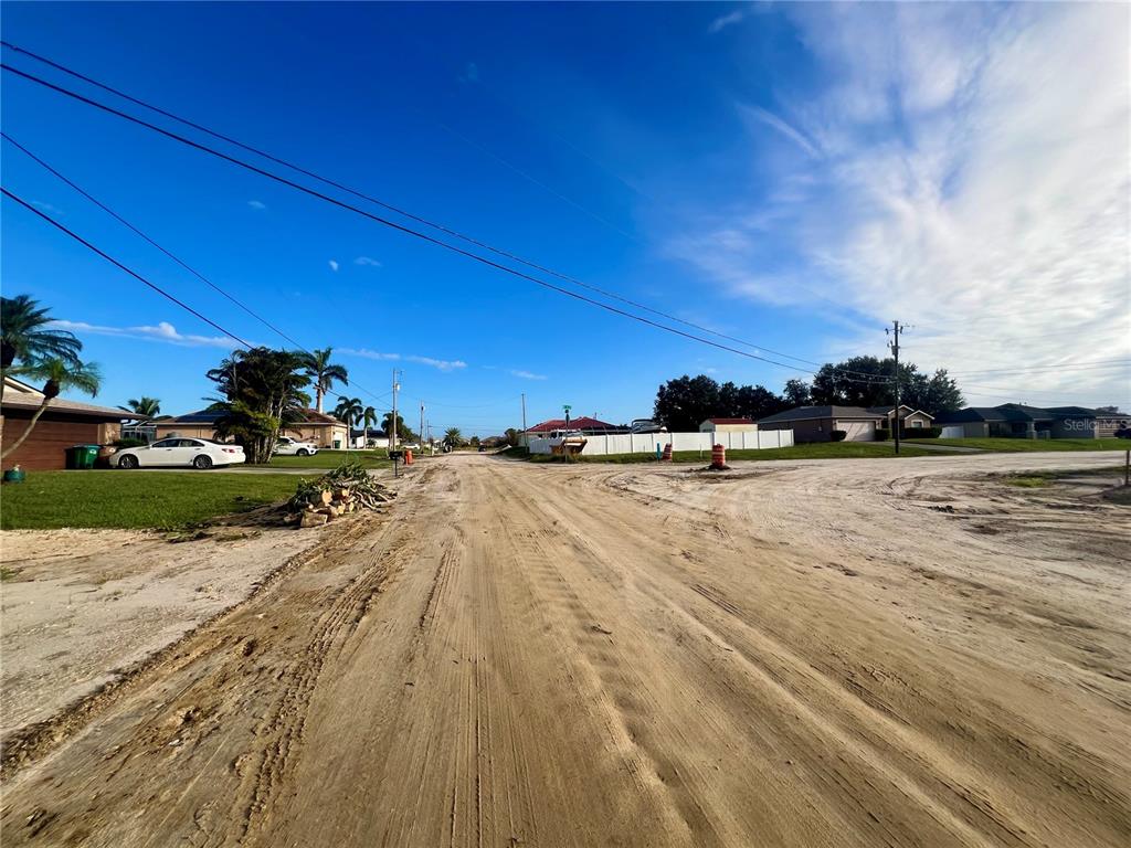 A dirt road leads through a residential neighborhood under a clear blue sky — 1424 NE 9TH AVENUE, CAPE CORAL, FL