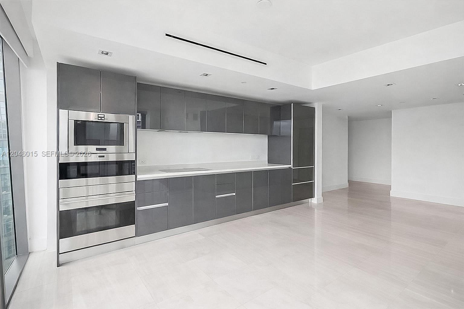 A modern kitchen features gray glossy cabinets, stainless steel appliances, and light-colored tile flooring — 1451 Brickell Ave # 1404, Miami FL 33131, MIAMI, FL