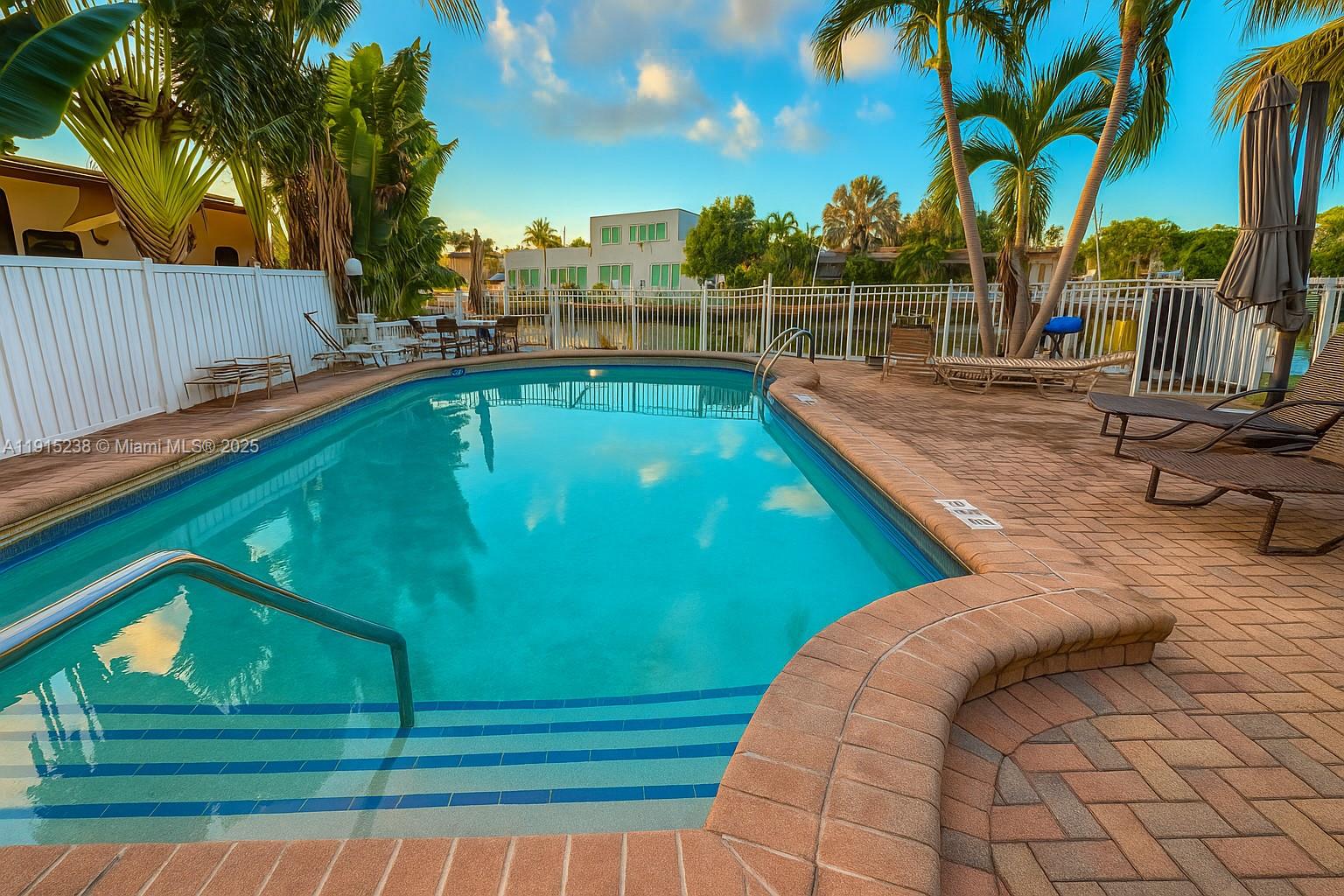 A backyard swimming pool with a brick deck, lounge chairs, and a white fence — 1100 Pine Dr # 106, Pompano Beach FL 33060, POMPANO BEACH, FL