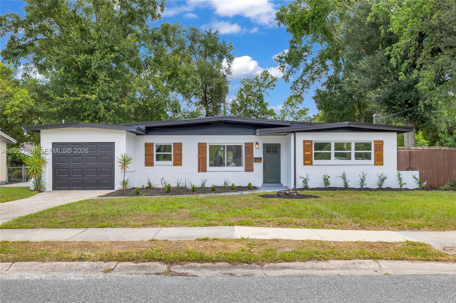 A single-story white house with a dark garage door, wood shutters, and a green door — ORLANDO, FL