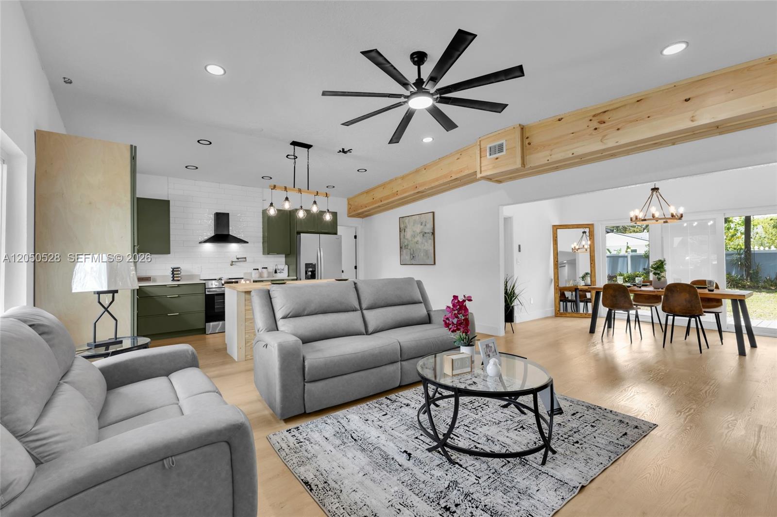 An open-concept living room and kitchen feature light wood floors, a ceiling fan, and beams — ORLANDO, FL