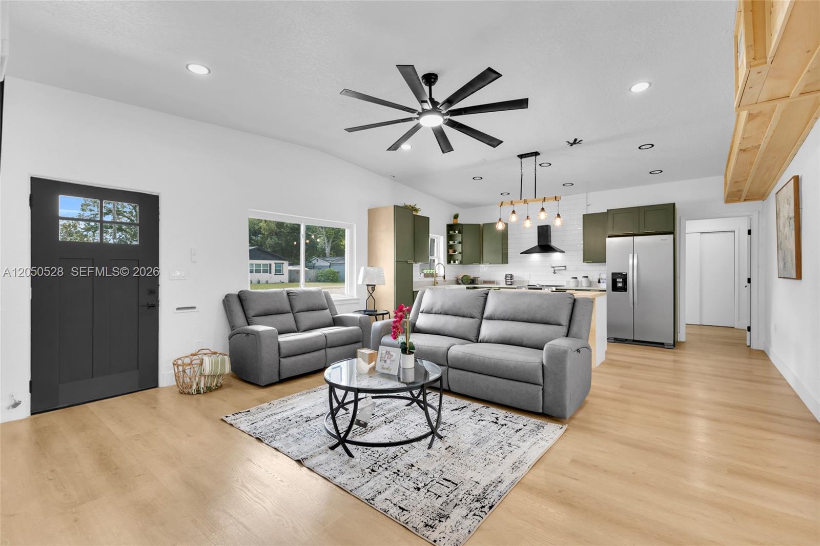 This open-concept living room features light wood flooring, gray furniture, and olive green kitchen cabinets — ORLANDO, FL