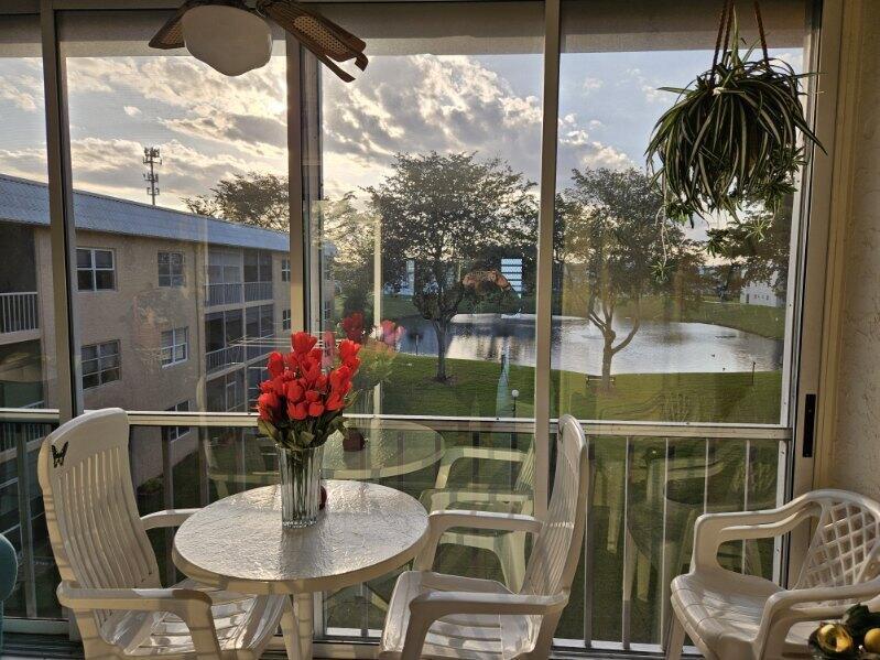 A screened-in balcony with white patio furniture, a vase of flowers, and a lake view — 9818 Marina Boulevard, Boca Raton FL 33428, BOCA RATON, FL