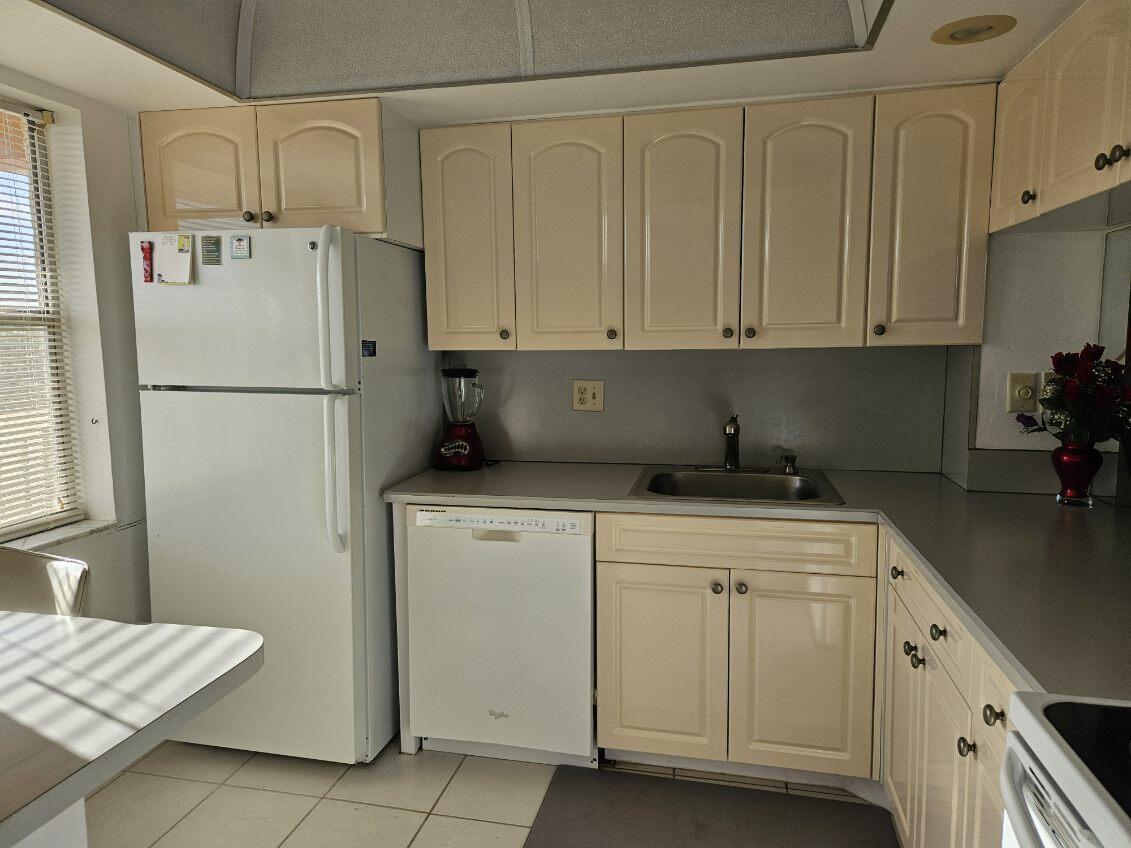 A kitchen with cream-colored cabinets, white appliances, a stainless steel sink, and tile flooring — 9818 Marina Boulevard, Boca Raton FL 33428, BOCA RATON, FL