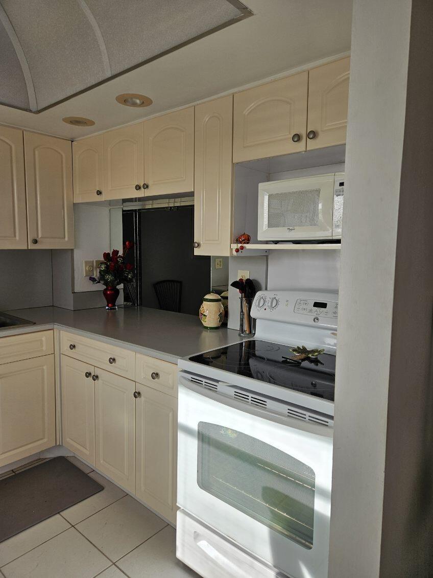 A kitchen features cream-colored cabinets, a white electric range, a microwave, and light-colored countertops — 9818 Marina Boulevard, Boca Raton FL 33428, BOCA RATON, FL