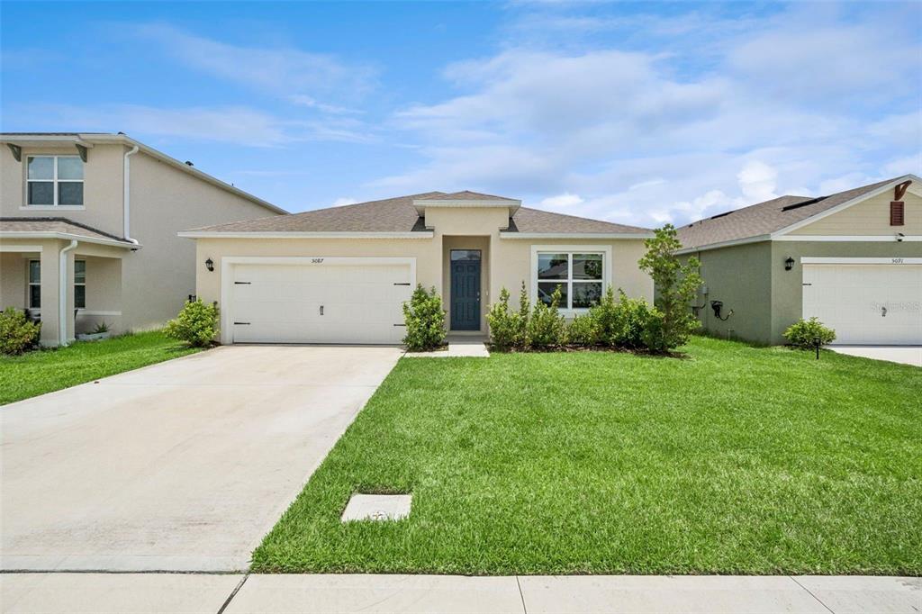 A single-story suburban house with a two-car garage, beige stucco siding, and a front lawn — 5087 TANA TERRACE, ST CLOUD, FL