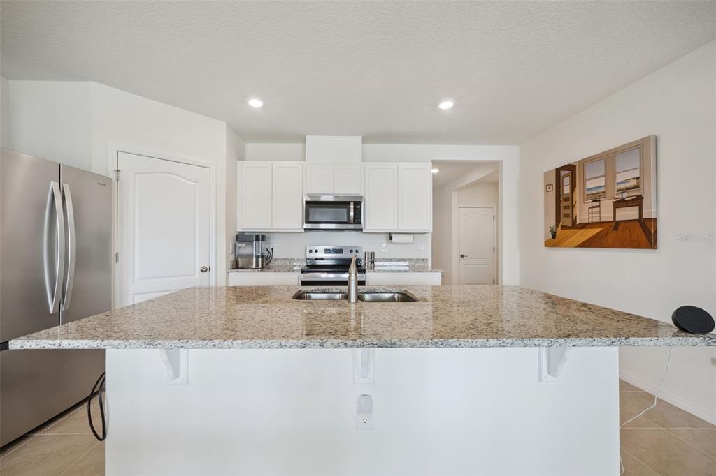 A kitchen features a granite-topped island with a sink, white cabinets, and stainless steel appliances — 5087 TANA TERRACE, ST CLOUD, FL