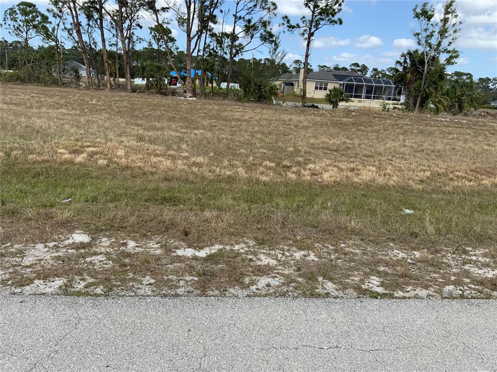 A vacant, grassy residential lot sits next to a house with a screened-in pool enclosure — 323 NE 31ST STREET, CAPE CORAL, FL