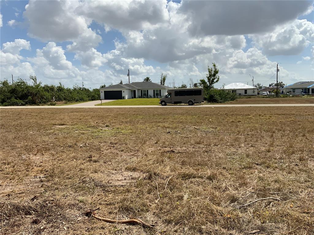 A vacant, grassy lot sits in the foreground across from a house and a parked bus — 323 NE 31ST STREET, CAPE CORAL, FL