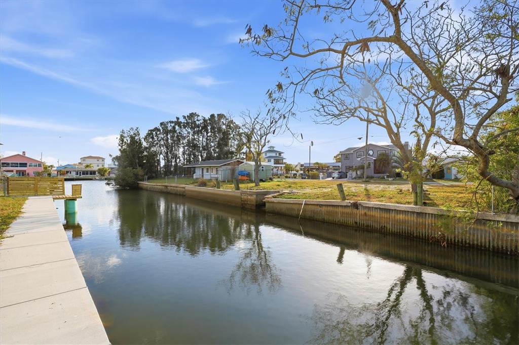 A concrete dock extends along a canal toward houses and trees under a blue sky — 14203 SHILOH COURT, HUDSON, FL