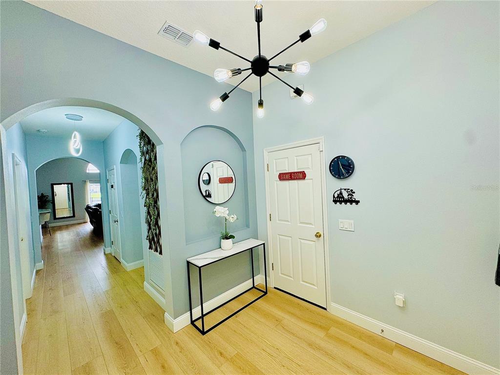 A foyer features light blue walls, wood-look flooring, a modern chandelier, and a console table — 4647 CUMBRIAN LAKES DRIVE, KISSIMMEE, FL