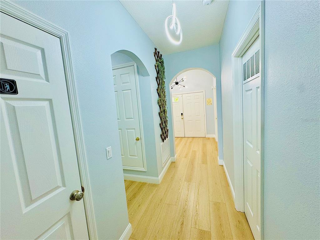 A hallway with light wood-look flooring, arched doorways, and white doors under a modern light — 4647 CUMBRIAN LAKES DRIVE, KISSIMMEE, FL